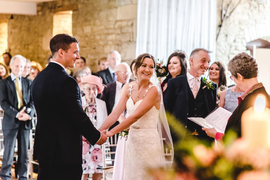 Bride holding grooms hands at a great tythe barn wedding ceremony