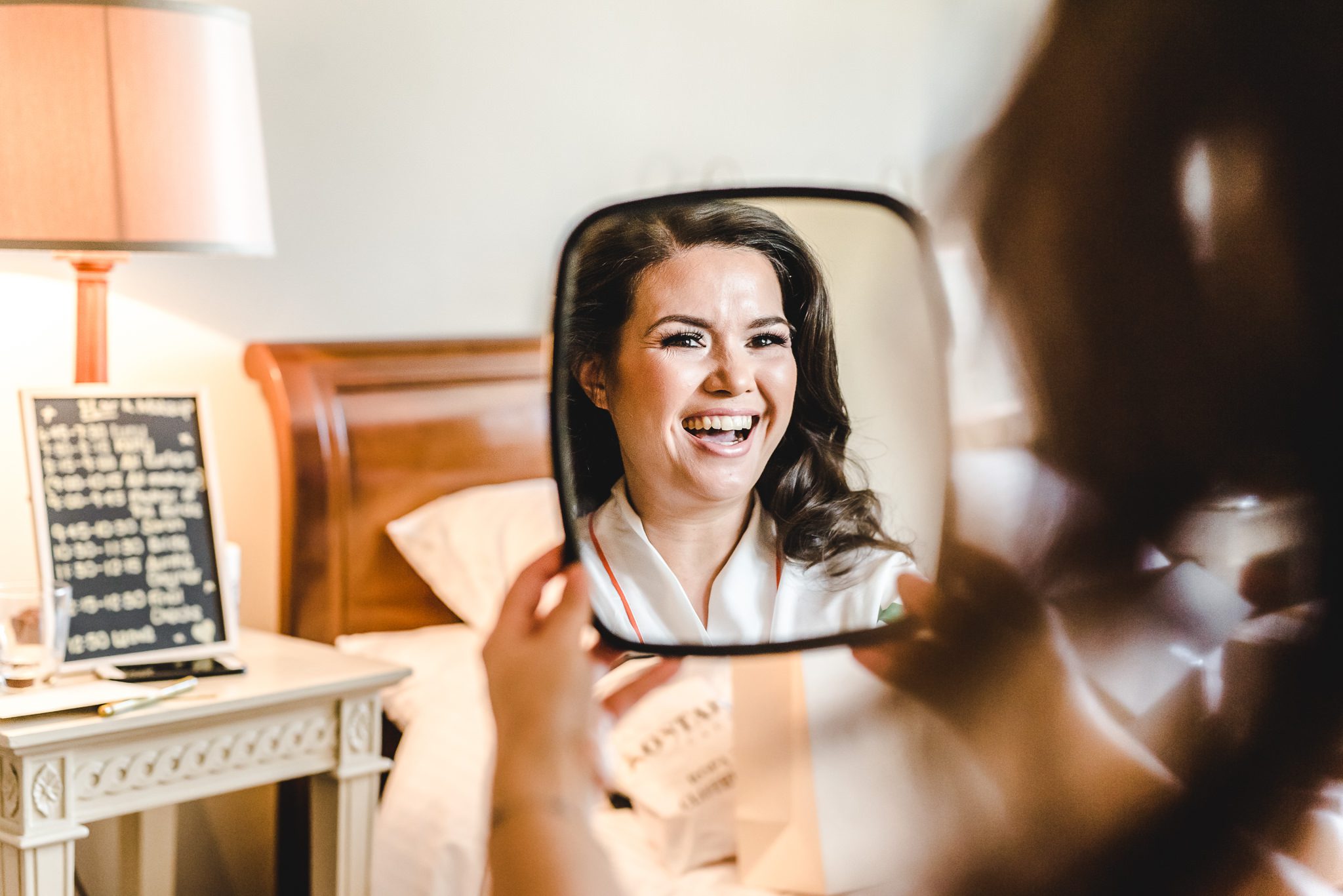 A Stone Barn bride smiling into a mirror before her wedding