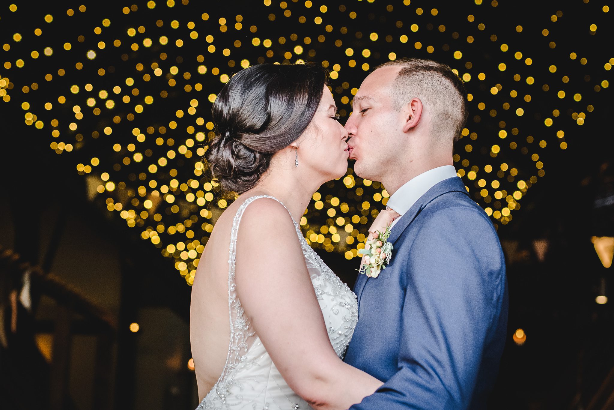 Bride and groom kissingbeneath a caopy of fairy lights at cripps stone barn