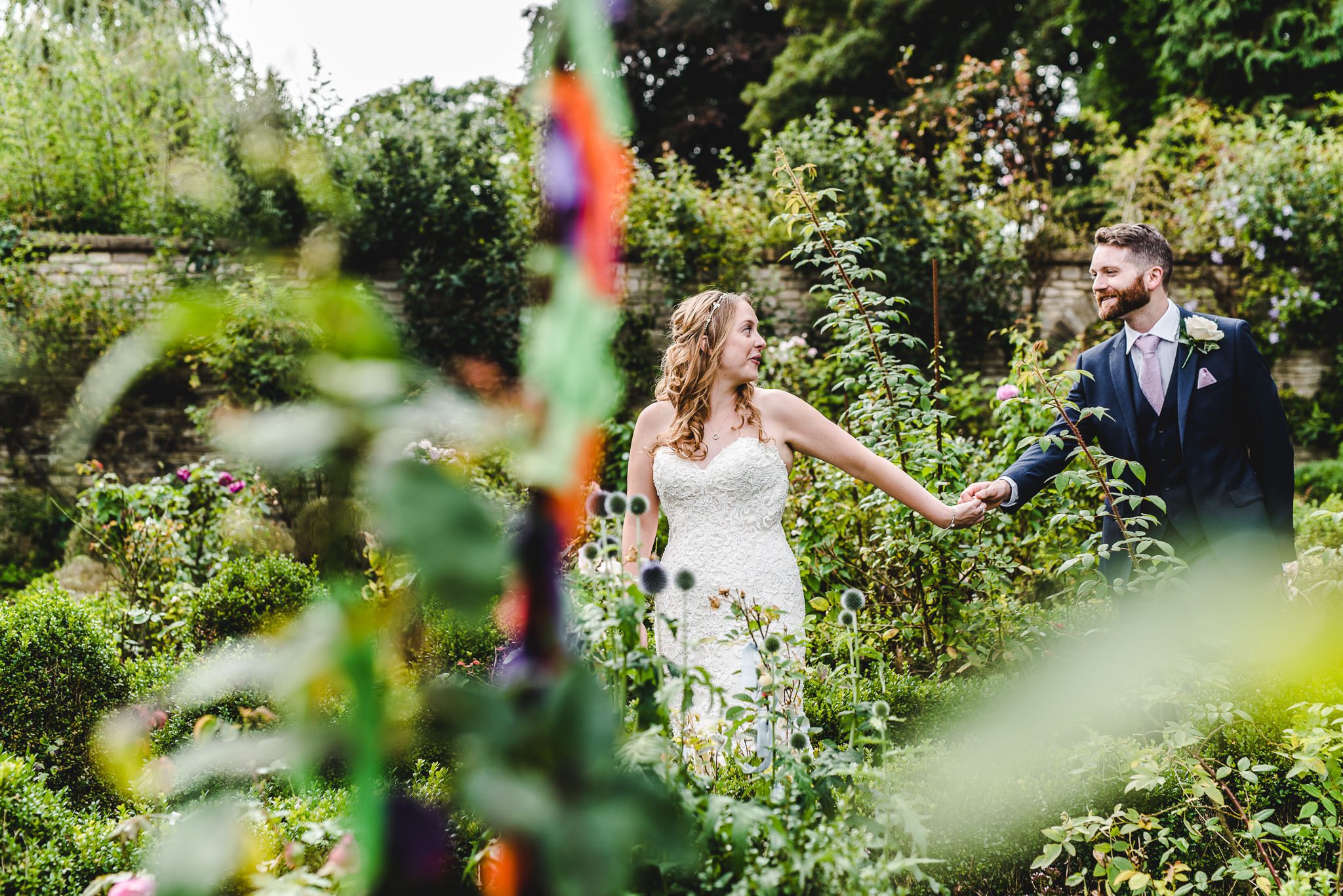 Bride leading groom out of a colourful garden