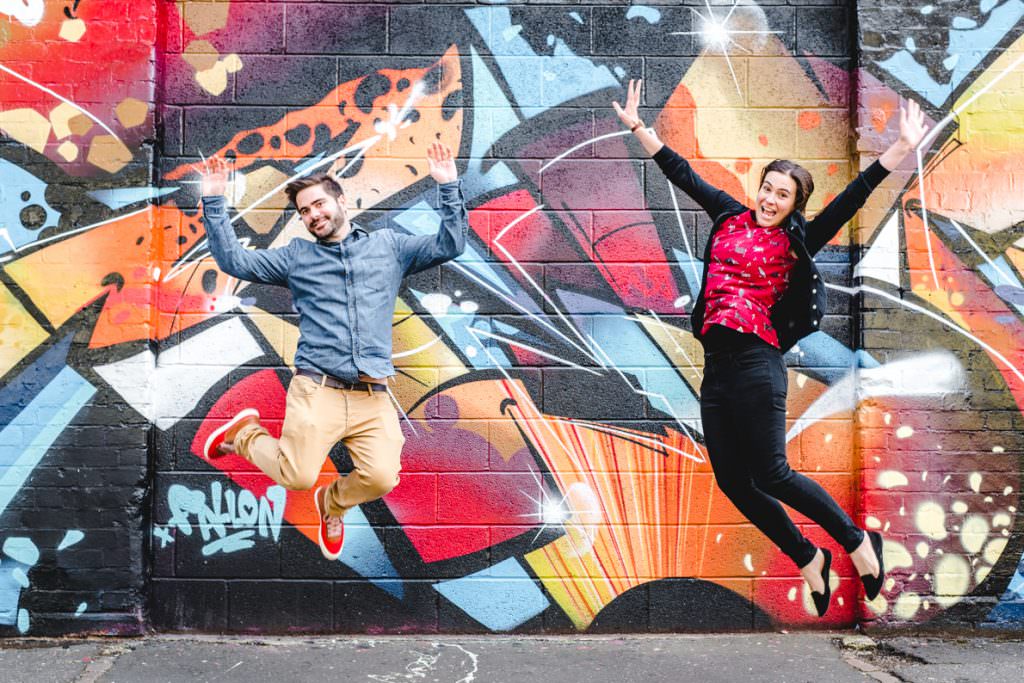A young couple jumping with their arms in the air against a graffiti background