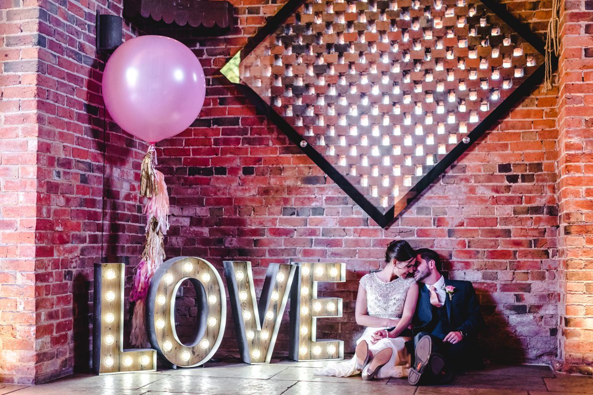 A couple seated by giant LOVE letters at a Shustoke Barn Wedding