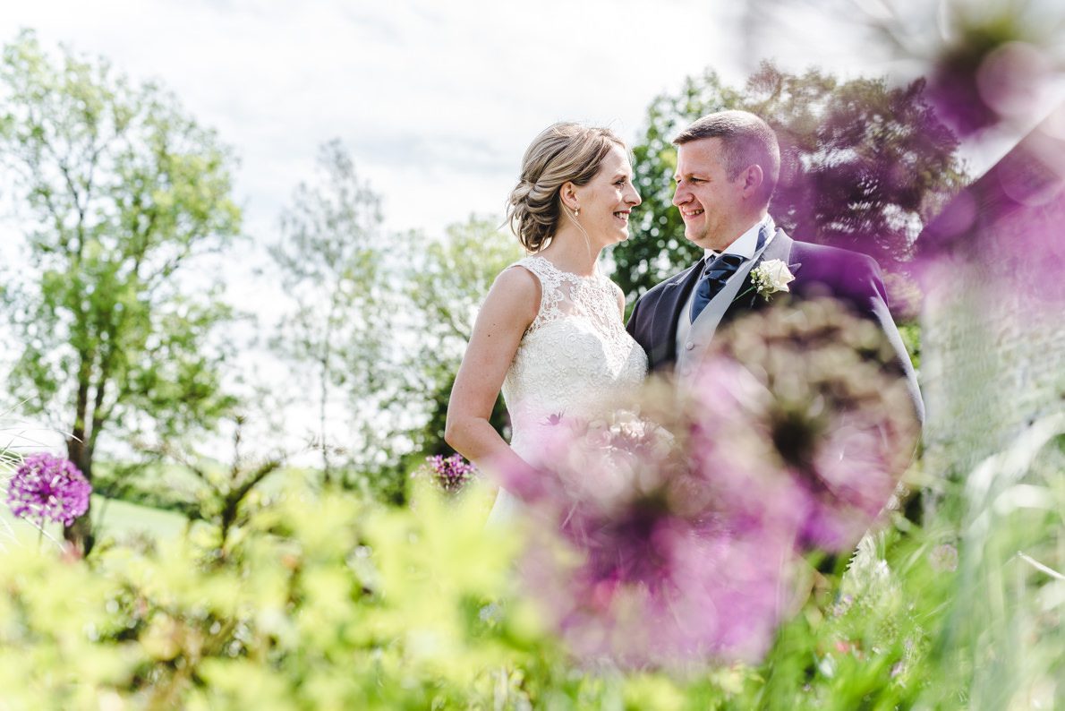Purple flowers in front of a Priston Mill couple at a wedding