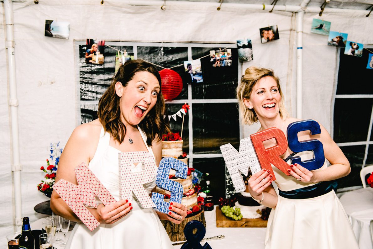 A couple holding up MRS and Mrs signs at their gay wedding