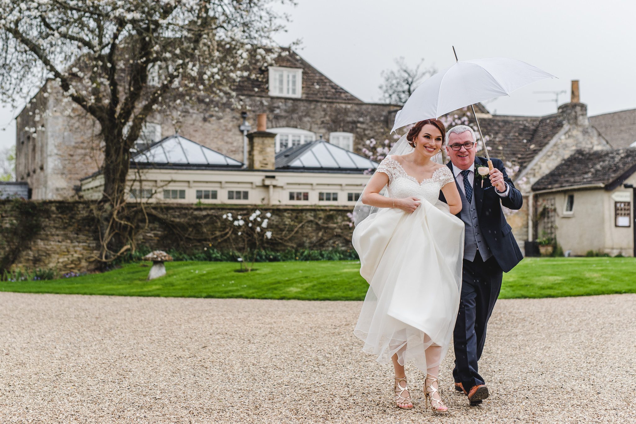 Bride and father walking with umbrella in tetbury before their wedding ceremony