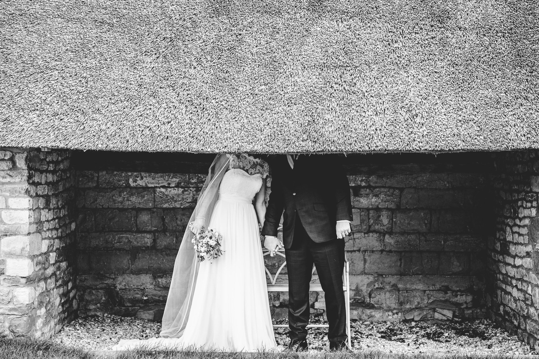 Bride and groom hiding behind a thatched roof