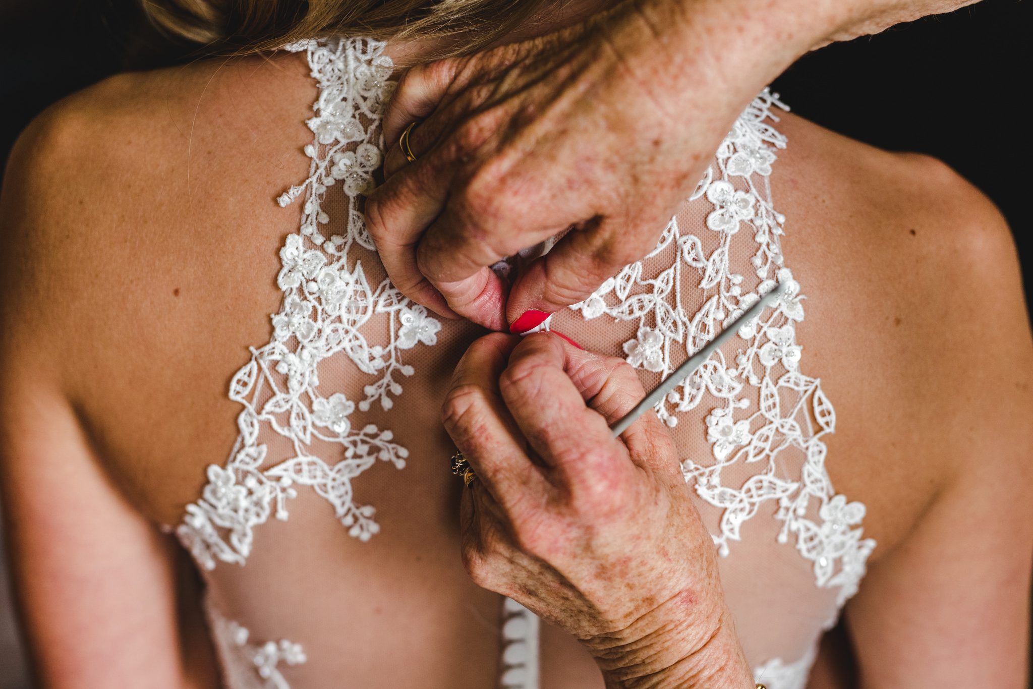 Bridesmaids and mum putting bride into dress