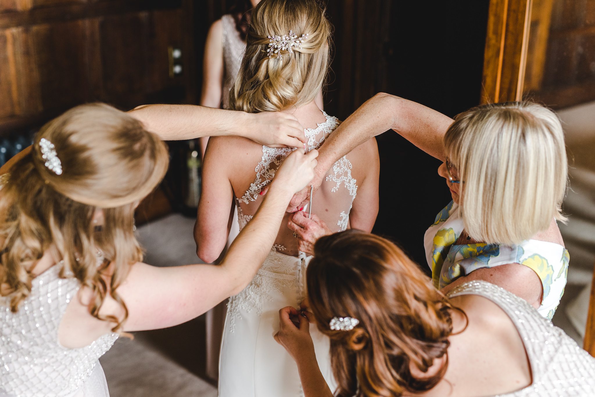 Bridesmaids and mum putting bride into dress