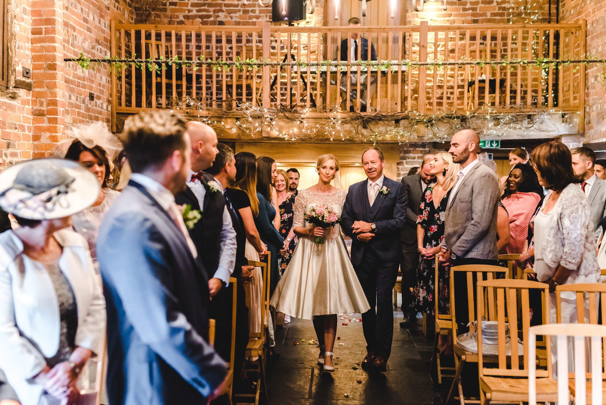 Bride walking the aisle to meet her groom at Curradine Barns