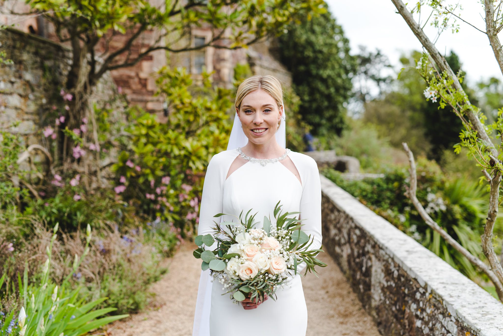 A bride standing in the gardens at Berkeley Castle with her flowers