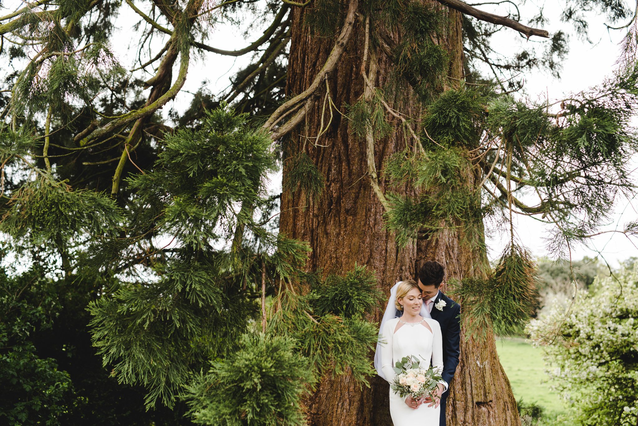 A bride and groom standing under a pine tree