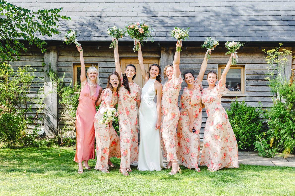 Bridesmaids in colourful dresses holding their bouquets in the air