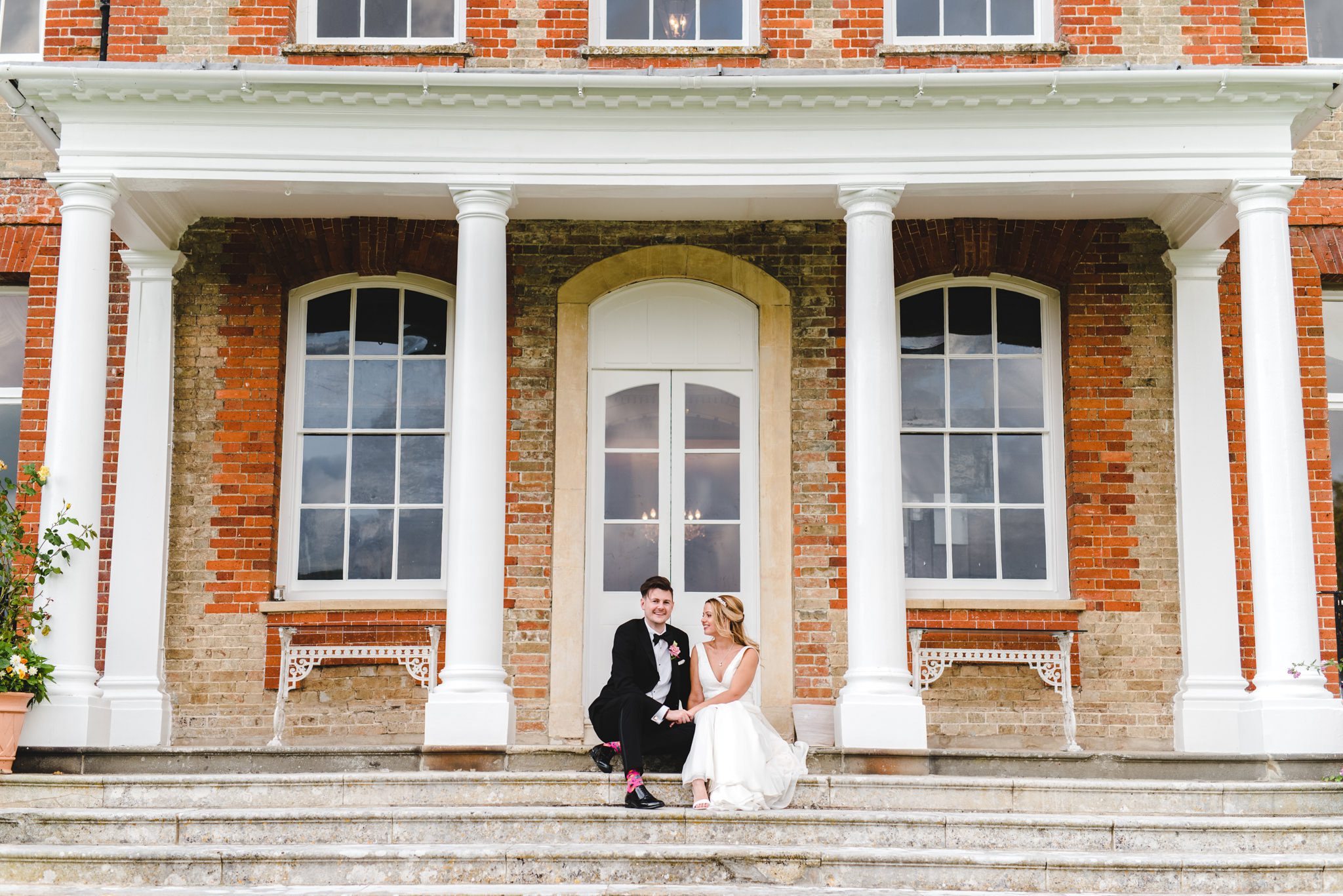 A bride and groom sat on the steps of Ardington House