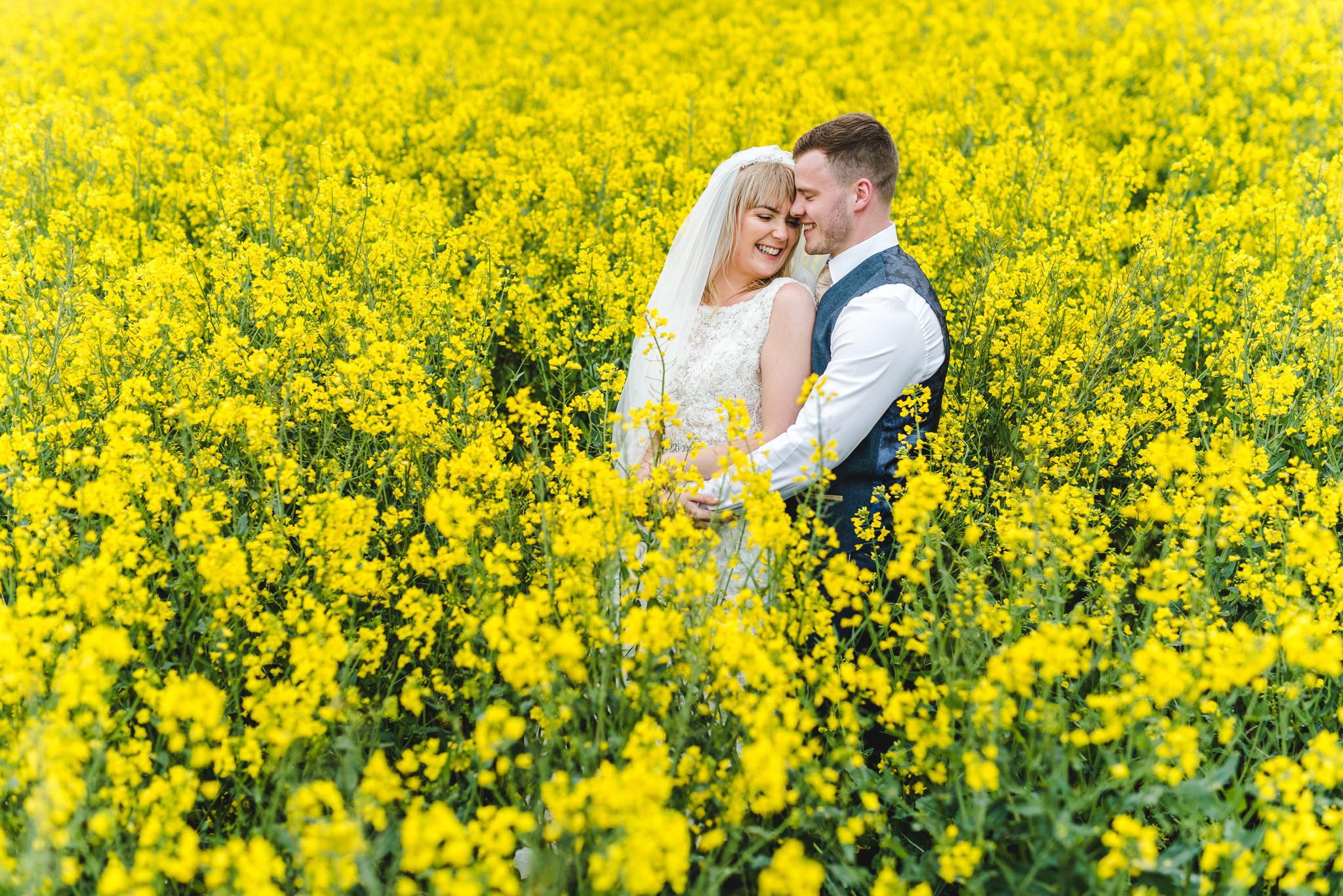 Bride and groom in an oilseed rape field at Kingscote Barn