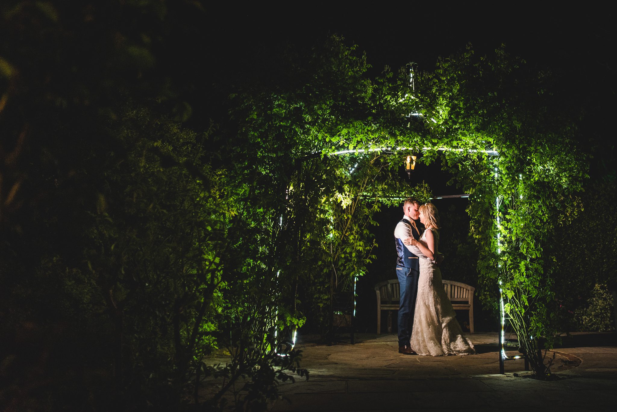 A couple standing under a fairy light arbor at their Kingscote Barn wedding