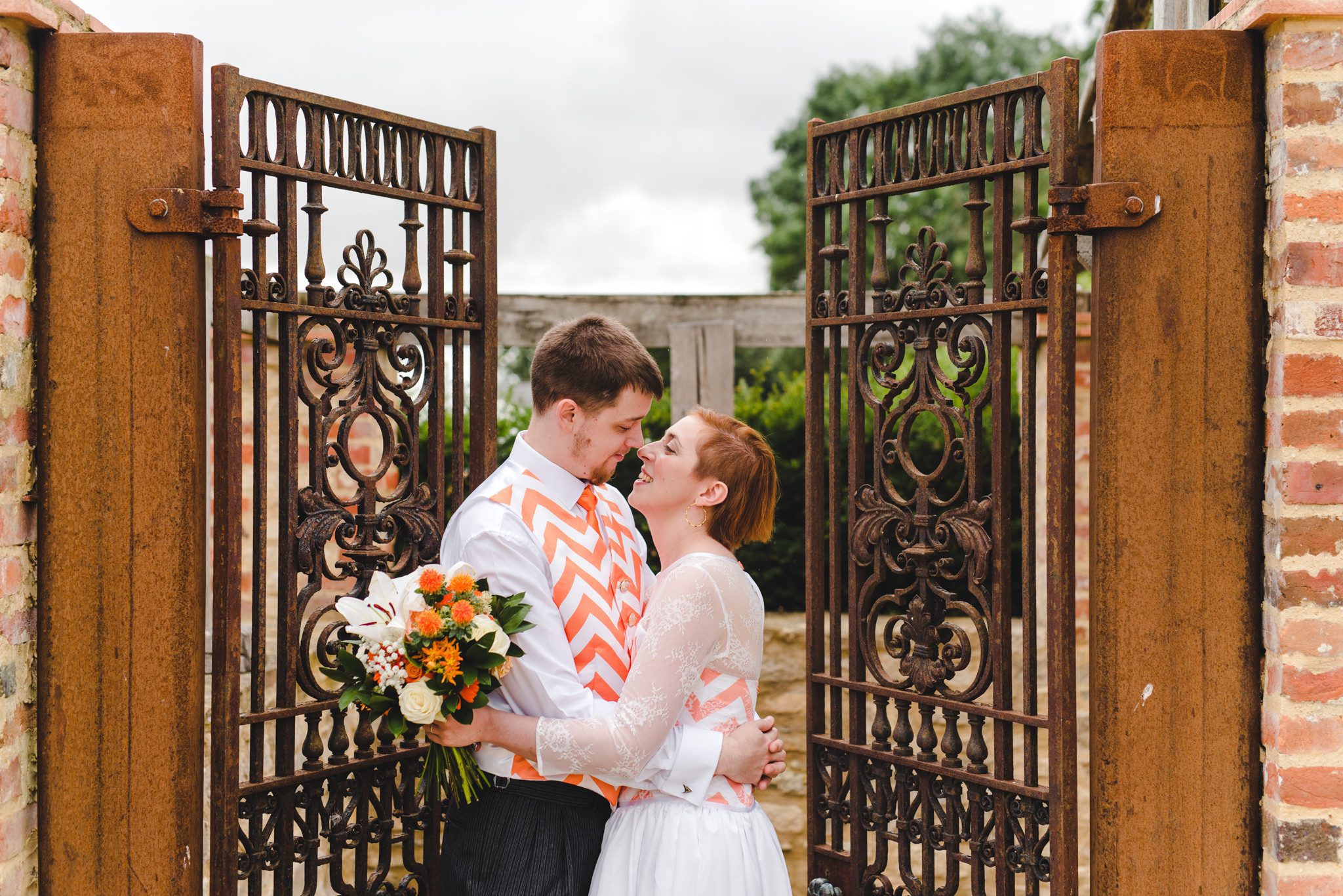 A couple close together by the main gates at Oxleaze Barn