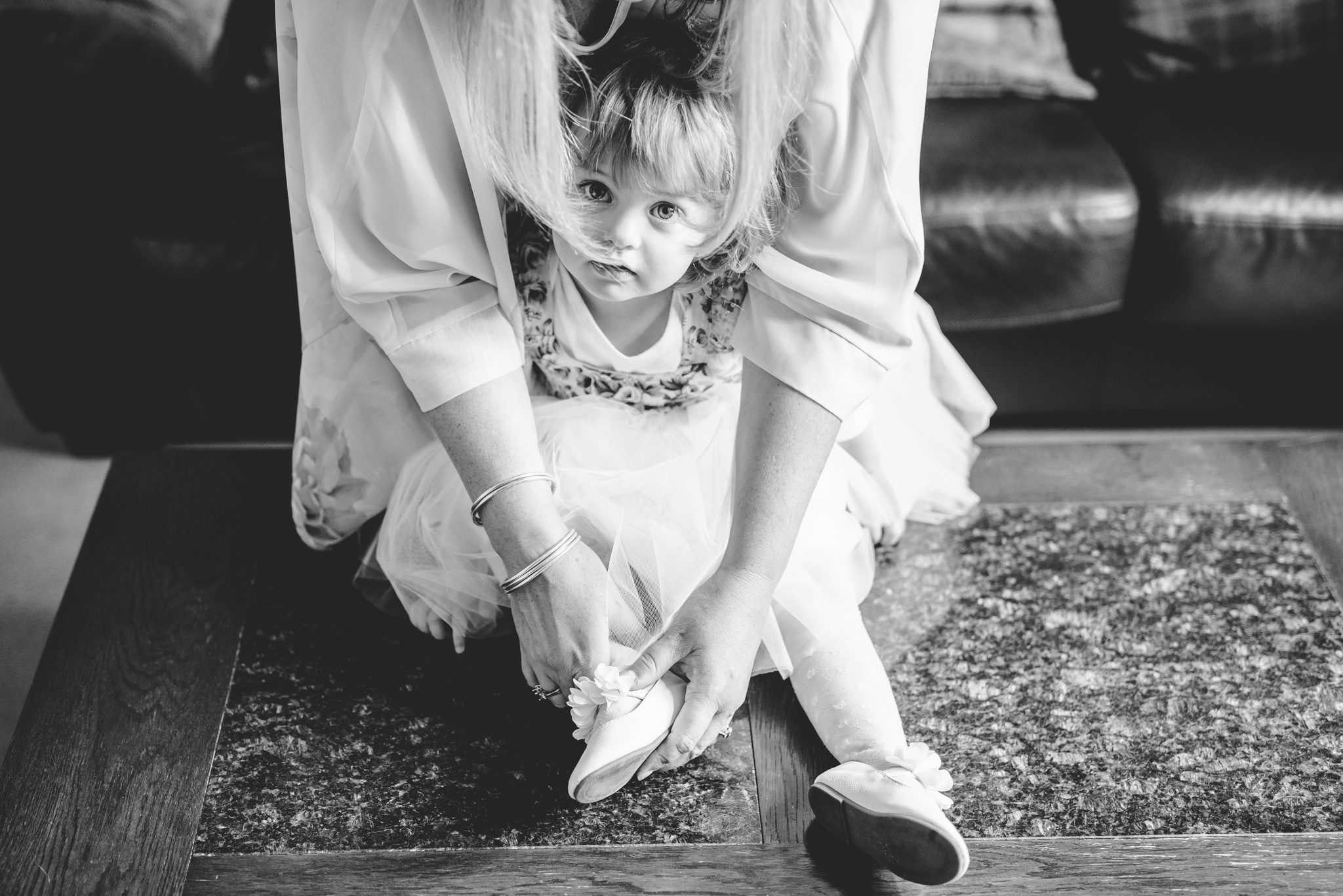 A black and white picture of a girl at a wedding having her shoes put on