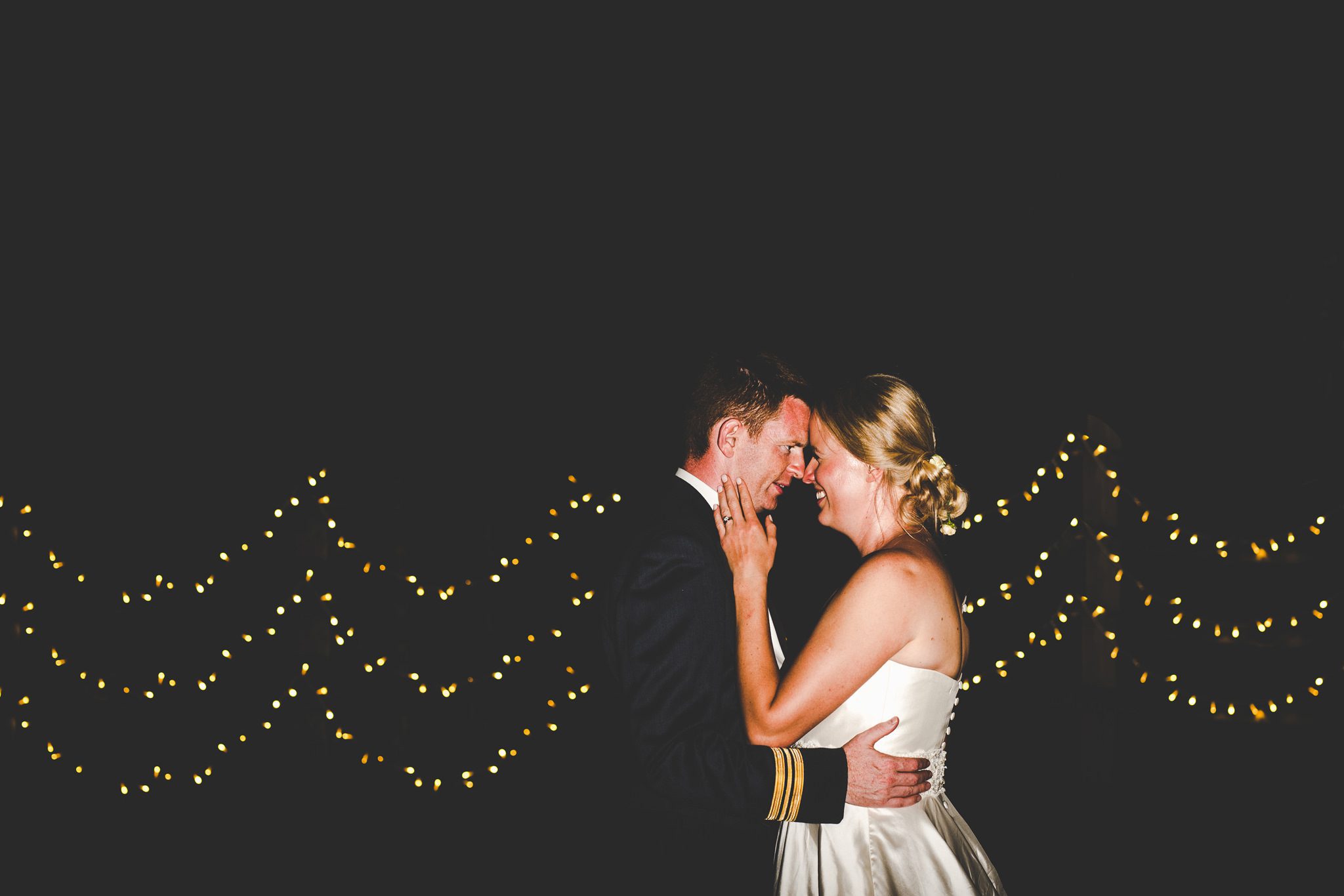 A night photo of a couple next to some fairy lights