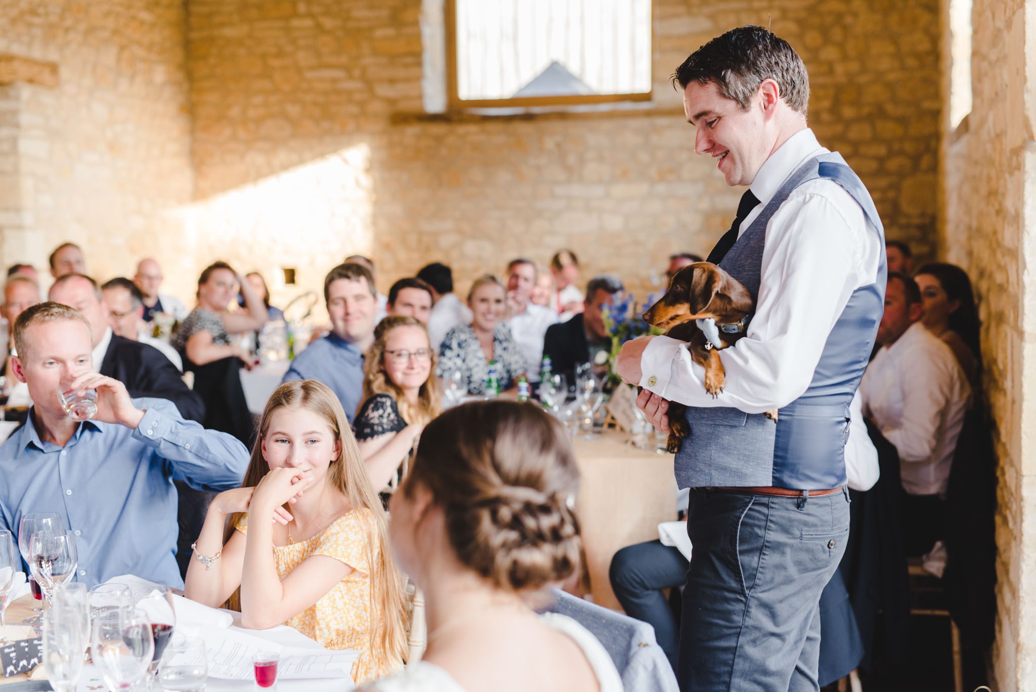 A groom delivering a speech holding his dachsund dog at Upcote Barn