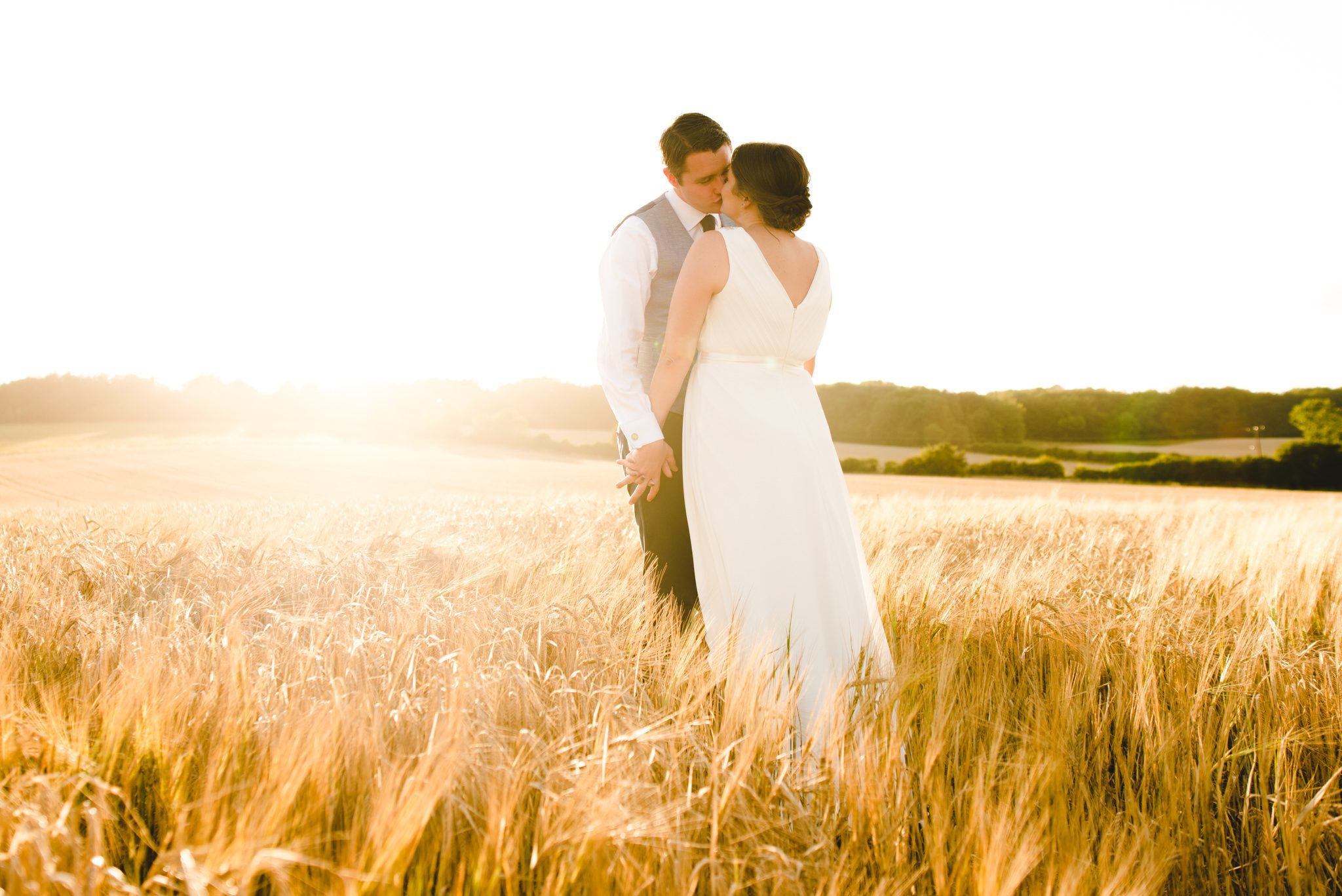 A bride and groom walking in a cornfield at The Barn at Upcote at sunset