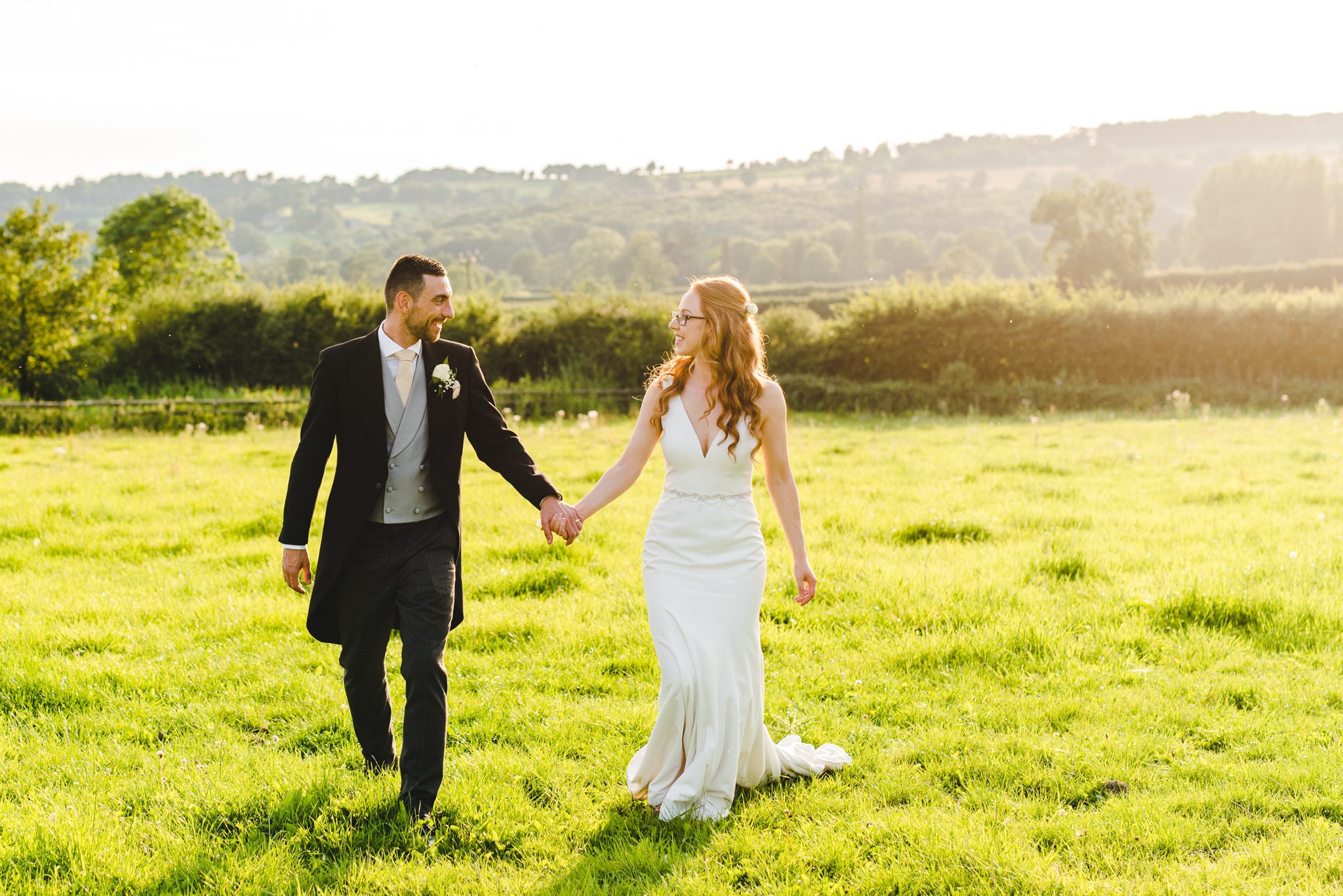 A bride and groom walking in the fields at sunset at Hyde House