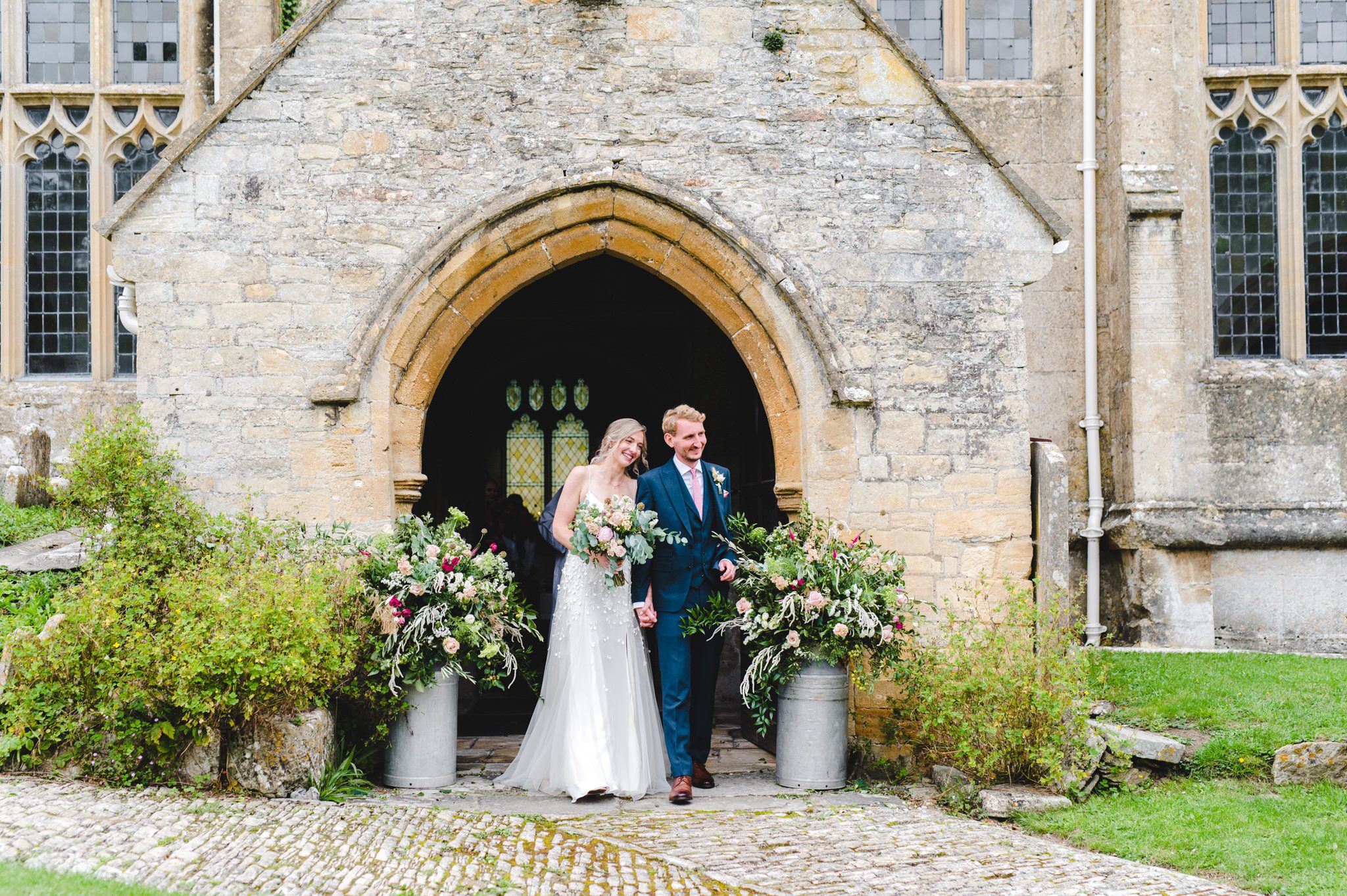 Bride and groom exiting Chedworth Church by Bigeye Photography