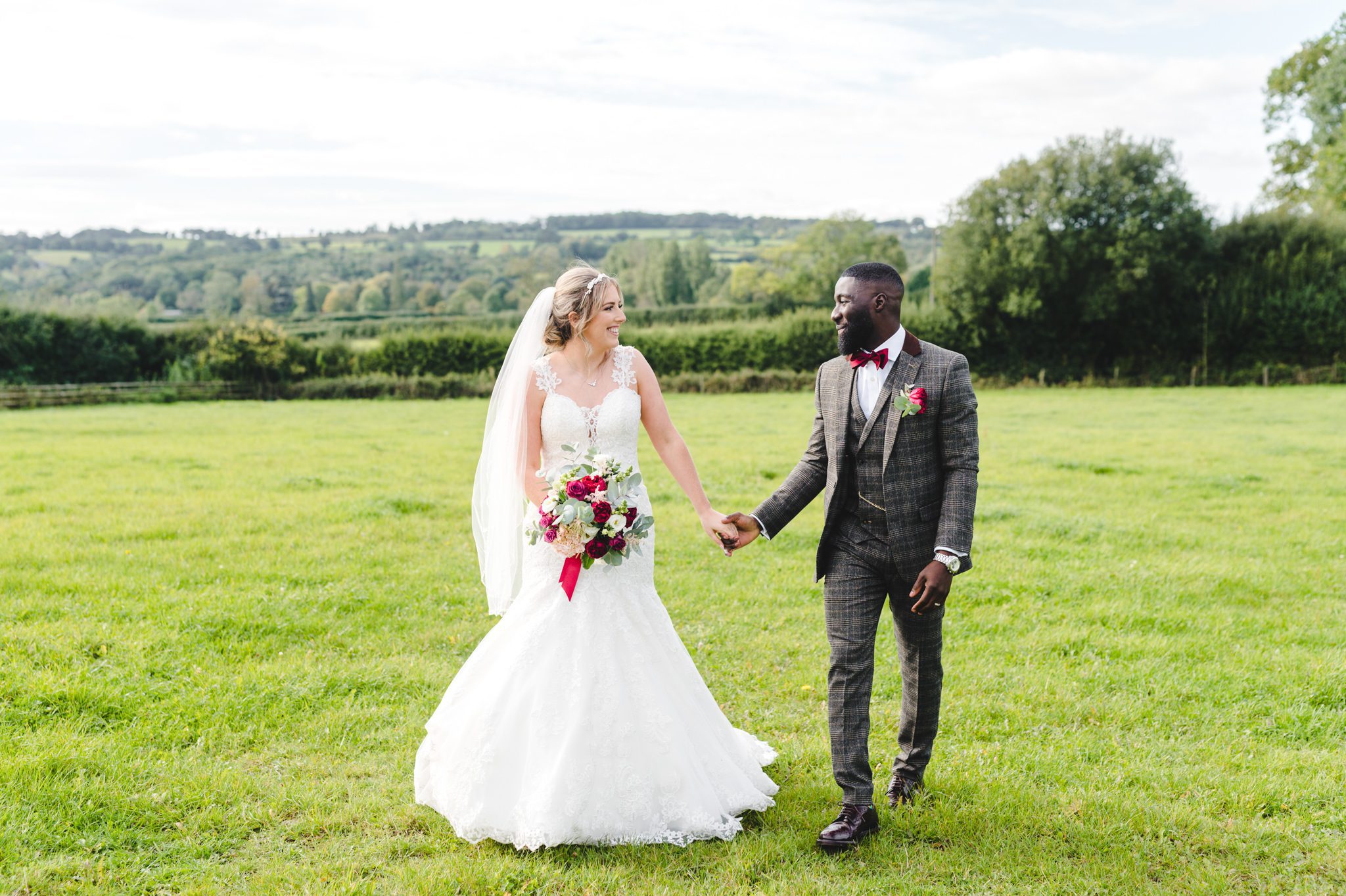 A bride and groom holding hands in a field at Hyde House on their wedding day