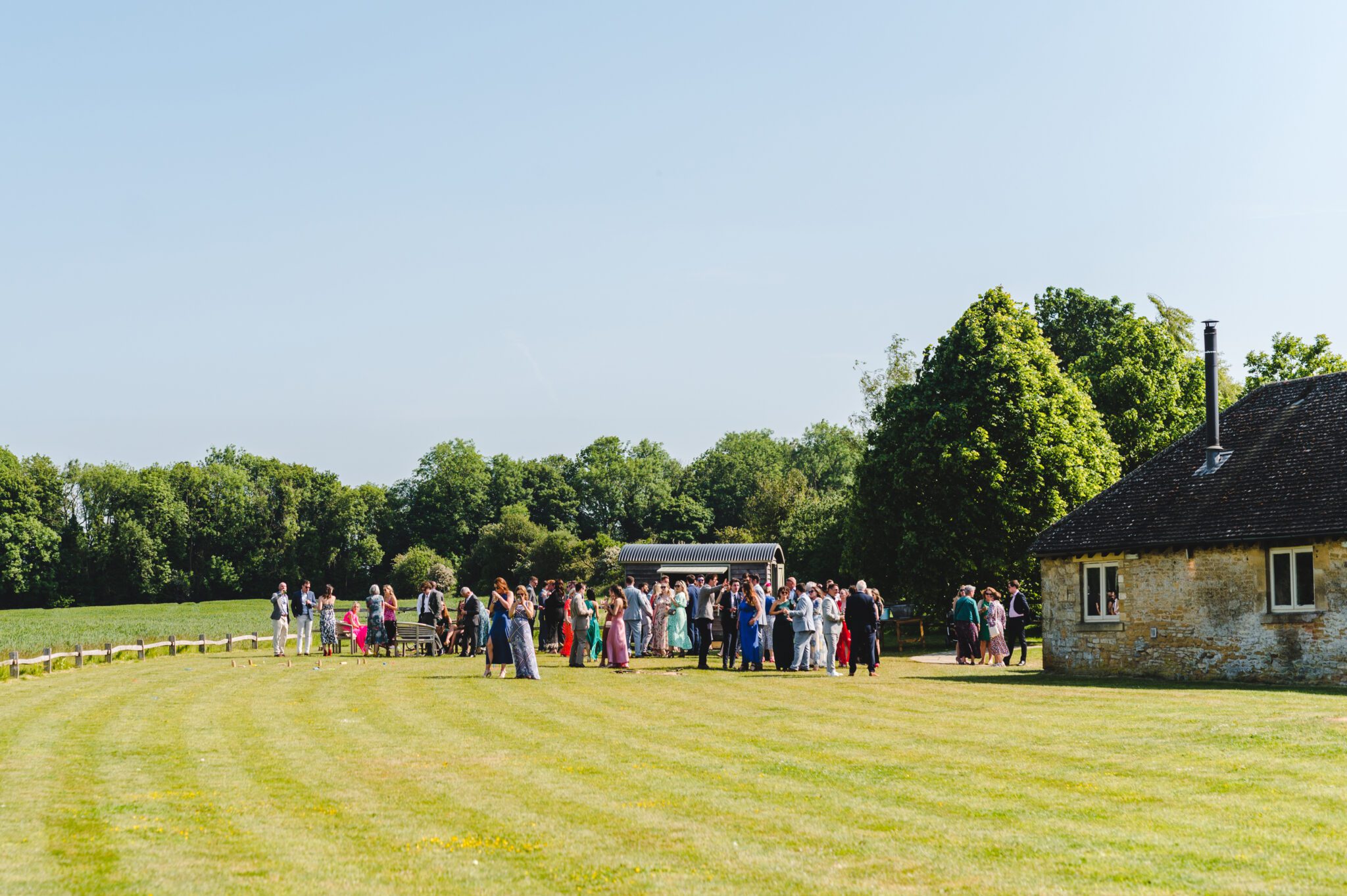 a wide view of lapstone barn with a drinks reception and blue skies in summer