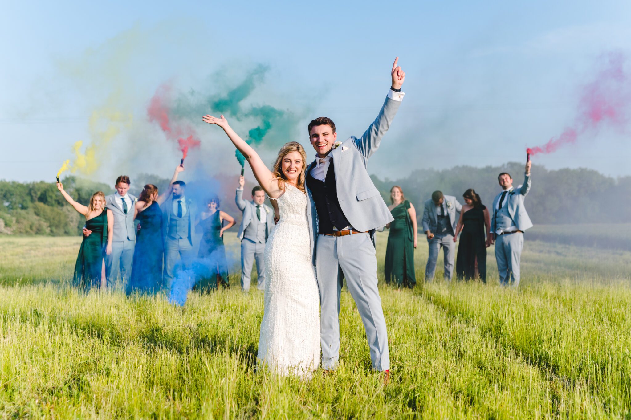 A happy bride and groom standing in front of their bridesmaids and groomsmen with arms aloft