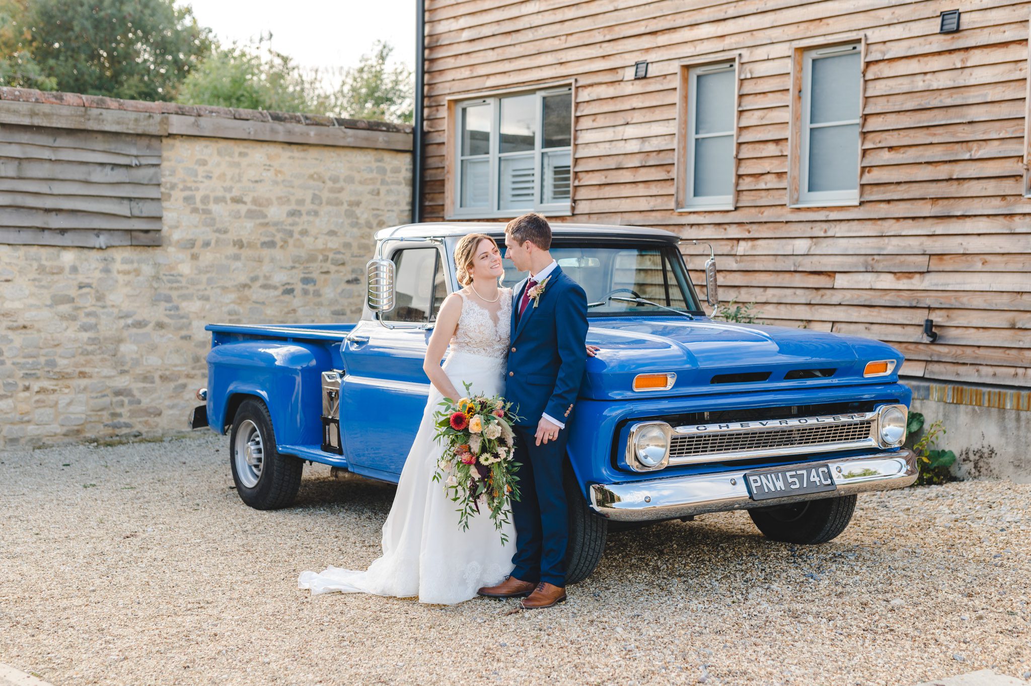 A bride and groom stood by their wedding car at Oxleaze Barn